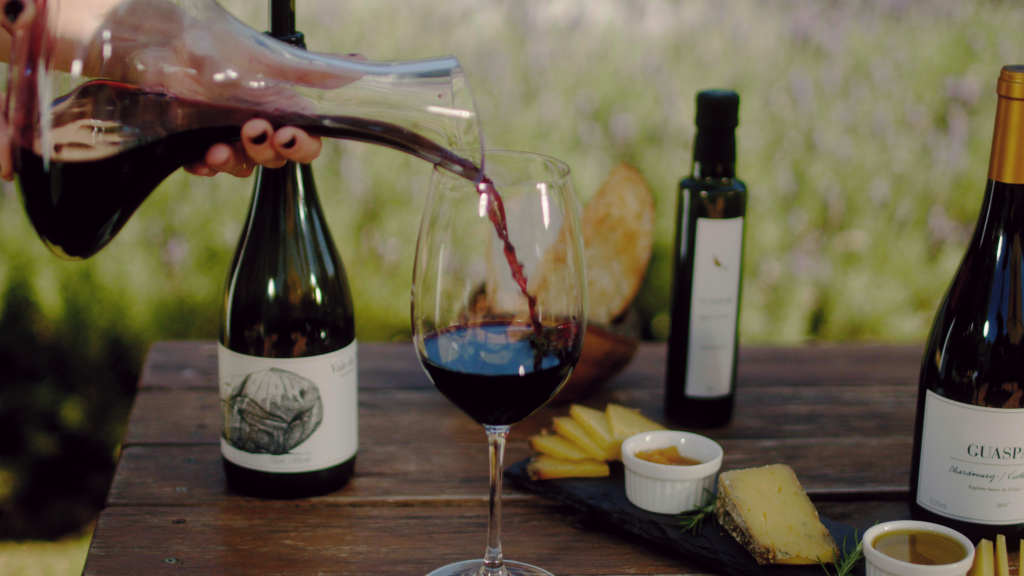 Vinho Vale da Pedra Syrah Tinto Guaspari é servido com decantador em mesa com queijos, geleia e azeite.